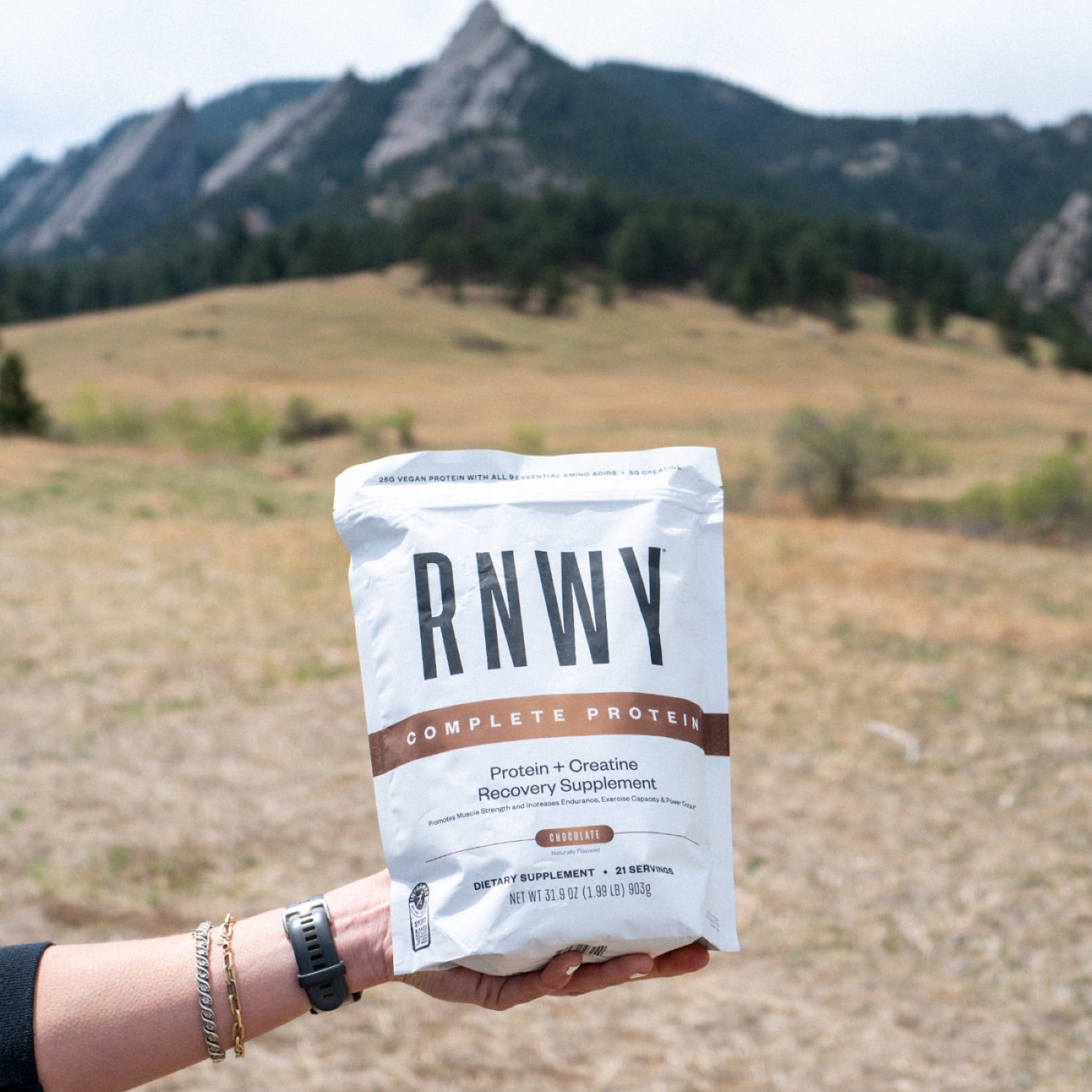 RNWY Complete Protein held outdoors against a mountain backdrop